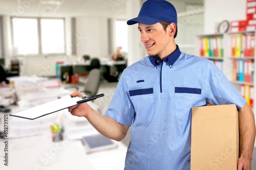Photo: Smiling delivery man, holding clip board and carton box Smiling delivery man, holding clip board and carton box