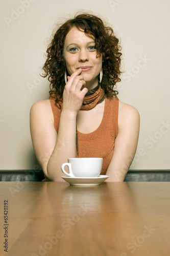 Photo: Junge Frau sitzt am Tisch mit Kaffeetasse Junge Frau sitzt am Tisch mit Kaffeetasse