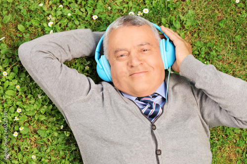 Photo: Mature man with headphones lying on grass Mature man with headphones lying on grass