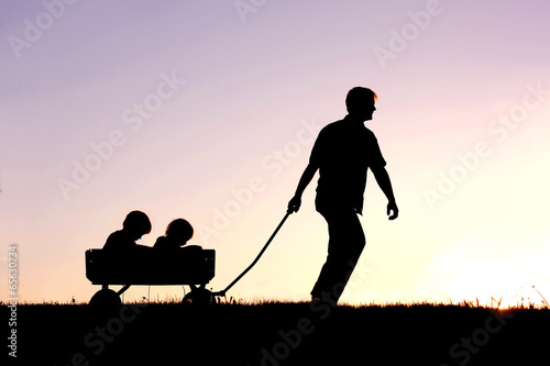 Photo: Silhouette of Father Pulling Sons in Wagon at Sunset Silhouette of Father Pulling Sons in Wagon at Sunset
