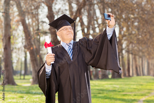 Photo: Mature graduate taking selfie in park Mature graduate taking selfie in park