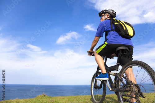 Photo: young man sitting on a mountain bike and looking the ocean young man sitting on a mountain bike and looking the ocean