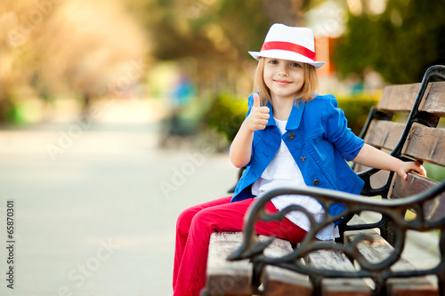 Photo: Portrait of little girl in a park showing thumb up Portrait of little girl in a park showing thumb up