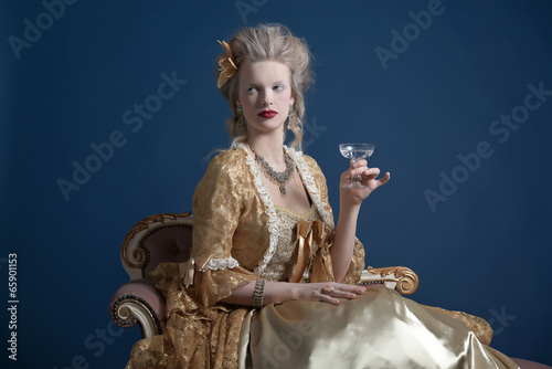 Photo: Retro baroque fashion woman wearing gold dress. Holding wine gla Retro baroque fashion woman wearing gold dress. Holding wine gla