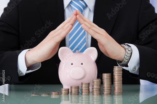 Photo: Businessman Sheltering Piggybank And Coin Stacks Businessman Sheltering Piggybank And Coin Stacks
