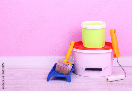 Photo: Paints, roll and paintbrush on floor in room on wall background Paints, roll and paintbrush on floor in room on wall background