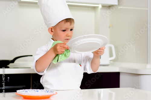 Photo: Cute young chef checking his dinner plates Cute young chef checking his dinner plates