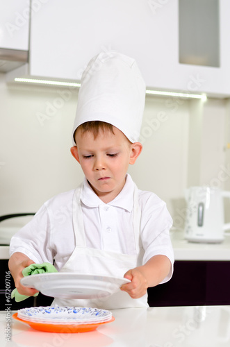 Photo: Little boy chef cleaning his plates while cooking Little boy chef cleaning his plates while cooking