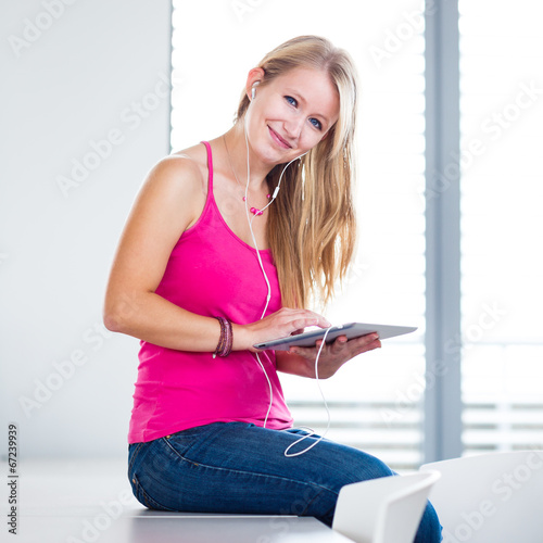 Photo: Pretty, young female student listening to music on her tablet Pretty, young female student listening to music on her tablet