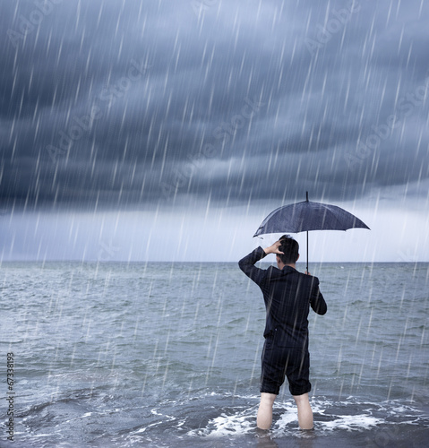 Photo: upset business man holding a umbrella with cloudburst background upset business man holding a umbrella with cloudburst background