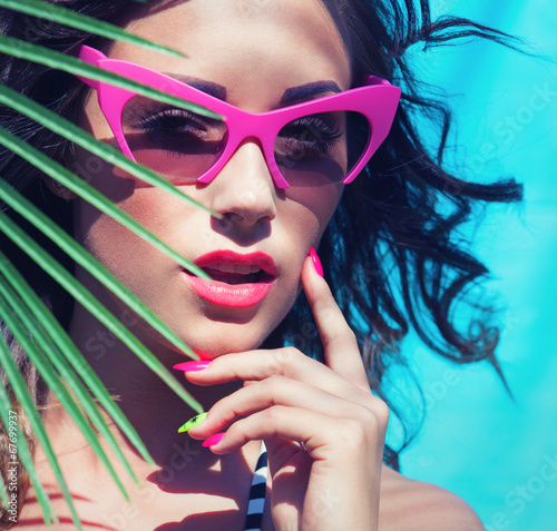 Photo: Young attractive woman wearing sunglasses under a palm tree Young attractive woman wearing sunglasses under a palm tree