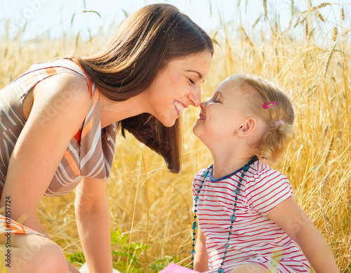 Photo: Happy young mother with little daughter on field in summer day Happy young mother with little daughter on field in summer day