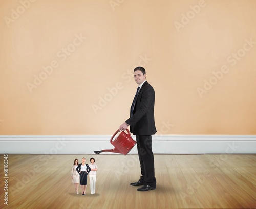 Photo: Composite image of businessman watering tiny businesswomen Composite image of businessman watering tiny businesswomen