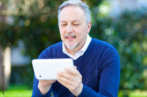 Photo: Senior man using a digital tablet outdoor in the park Senior man using a digital tablet outdoor in the park