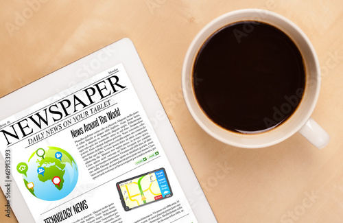 Photo: Tablet pc shows news on screen with a cup of coffee on a desk Tablet pc shows news on screen with a cup of coffee on a desk