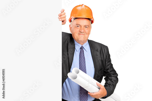 Photo: Mature construction worker standing behind panel Mature construction worker standing behind panel