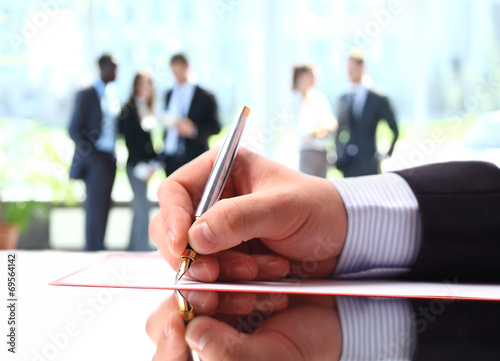 Photo: Hands writing on a paper while business team discussing Hands writing on a paper while business team discussing