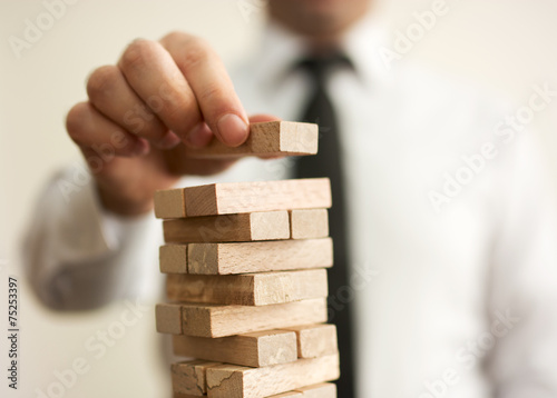 Businessman putting last block to the tower
