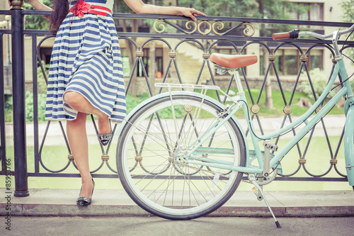 Young girl dressed in a striped dress standing near fence, near vintage city bike at the park. Freedom woman with her happy vacation travel at European city, Paris Photo by petunyia