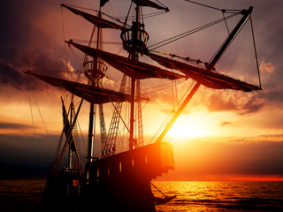 Old ancient pirate ship on peaceful ocean at sunset.
