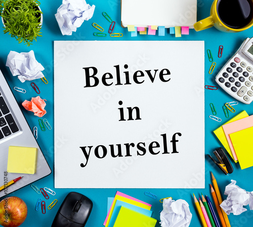 Believe in yourself. Office table desk with supplies, white blank note pad, cup, pen, pc, crumpled paper, flower on wooden background. Top view Photo by projectio
