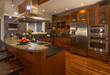 Contemporary upscale home kitchen interior with wood cabinets and floors, granite countertop, accent lighting, television & stainless steel appliances including double oven, refrigerator and vent hood Contemporary upscale home kitchen interior with wood cabinets and floors, granite countertop, accent lighting, television & stainless steel appliances including double oven, refrigerator and vent hood