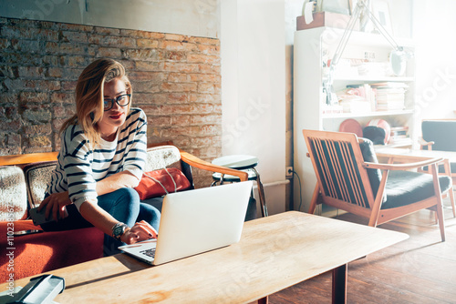 Beautiful young blonde female student using portable laptop computer while sitting in a vintage coffee shop.Young beautiful girl using a personal laptop computer to look up information on the internet