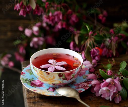 fruit tea in a cup and pink flowers on a wooden background © venge
