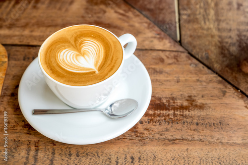 Close up white coffee cup with heart shape latte art on wood tab