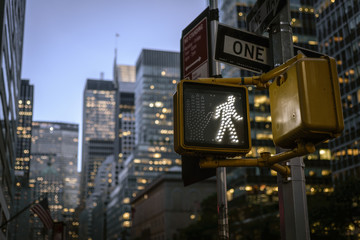 NYC crosswalk sign on busy one way street with sunset skyline in the background.