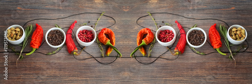 Concept of hot spice cuisine and seasoning - peppers, herbs, condiment. Black pepper, pink pepper, cardamon seeds, thyme, rosemary and chili peppers on wooden table. Wide panorama, horizontal