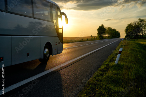 Zdjęcie XXL Biały autobus jazdy wzdłuż drogi asfaltowej w wiejski krajobraz o zachodzie słońca.