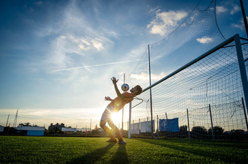 Football player is training at the field on a sunset background
