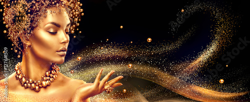 Golden woman. Beauty fashion model girl with golden make up, hair and jewellery on black background