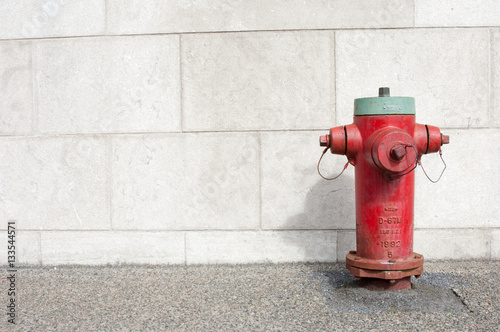 Red and green fire hydrant next to a light concrete wall on the sidewalk in Montreal, Quebec, Canada.  Copy space on the left.