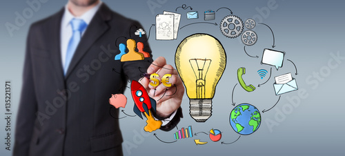 Businessman drawing a lightbulb with a pen with multimedia icons