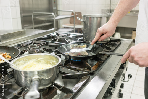 Fotoobraz na płótnie Szef kuchni lub szef kuchni w restauracji jest smażenie ryb karpiowatych w patelni na piecu