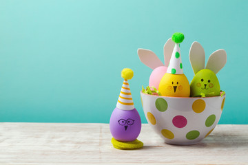 Easter holiday concept with cute handmade eggs, bunny, chicks and party hats in bowl on wooden table