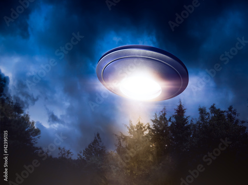 Fotoobraz na płótnie Wysoki kontrast obrazu UFO lecący nad lasem z wiązki światła w nocy