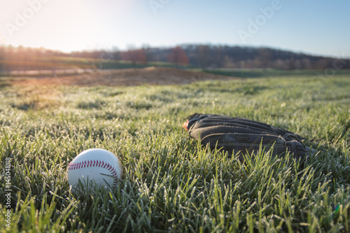 Fotoobraz na płótnie Baseball rękawiczka i piłka na polu w wczesnym poranku trawie i rosie gdy słońce wzrasta w tle