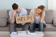 Worried Couple Holding Help Sign While Calculating Bills Worried Couple Holding Help Sign While Calculating Bills