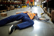 Fallen worker lying on the floor in aisle between storage shelves Fallen worker lying on the floor in aisle between storage shelves