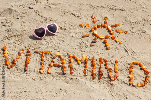 Фото: Sunglasses, inscription vitamin D and shape of sun at beach, concept of summer time and healthy lifestyle Sunglasses, inscription vitamin D and shape of sun at beach, concept of summer time and healthy lifestyle