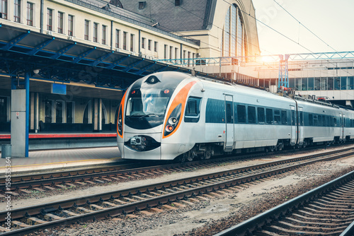 Plakat Wysoki prędkość pociąg przy stacją kolejową przy zmierzchem w Europa. Nowoczesny pociąg intercity na peronie kolejowym. Przemysłowy krajobraz z pociągiem pasażerskim na linii kolejowej. Transport kolejowy. Lokomotywa