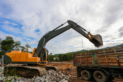 Plakat Ekskawator lub backhoe przy budową z niebieskim niebem i zmierzchem, ciężkim przemysłem i bezpieczeństwem przy pracy pojęciem ,.
