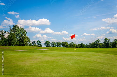 Plakat Pole golfowe z piękną zieloną trawą, błękitnym niebem i białymi chmurami puffy. Rekreacyjna aktywność sportowa w golfie.