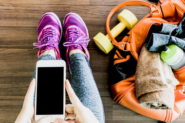 Woman holding smartphone with fitness equipment