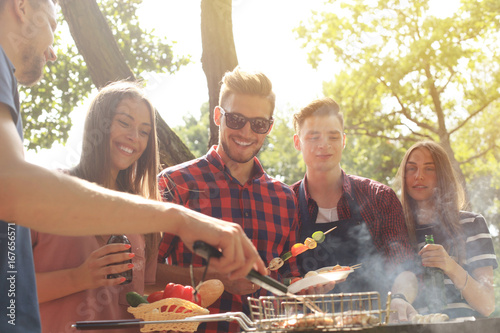 Plakat Szczęśliwi przyjaciele piec na grillu mięso i cieszyć się grilla przyjęcia outdoors.