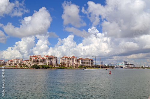 Plakat Luksusowe kondominium na wyspie, port Miami dźwigi załadunkowe i daleko Miami. sylwetka na tle nieba.