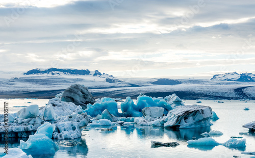 Plakat Lodowata laguna w Iceland, chmurna pogoda, góry na horyzoncie. Jezioro polodowcowe odbija niebo